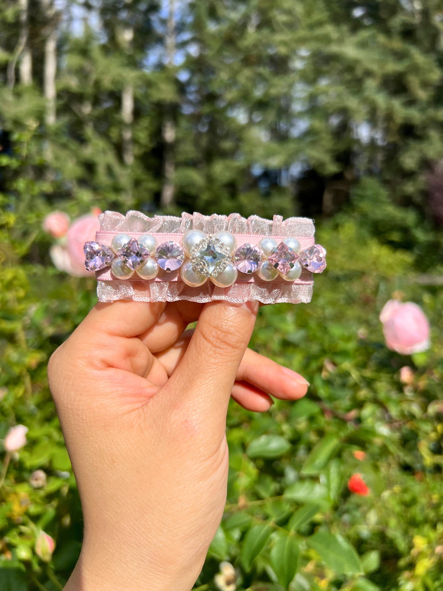model holding hair clips with Swarovski crystals and pearls embellished and silky organza with flowers against a green secrect garden background. Only at petite murmure