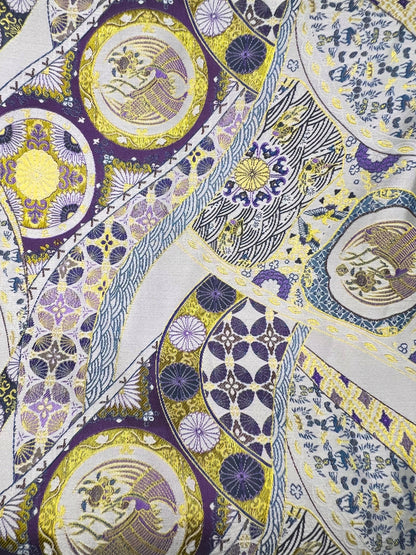 Close-up of a patterned fabric with circular designs in purple, yellow, and white to make the Exclusive Song brocade mulberry silk scrunchie with peony aromatic scent, infused with gold thread. Phoenix patterned scrunchie