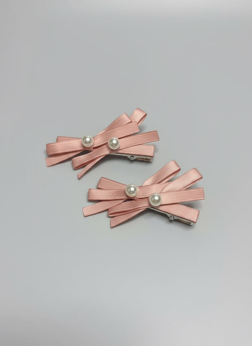 Pair of pink hair clips with layered bows and pearl centers on a clean background