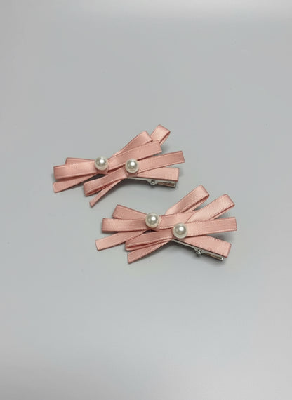 Pair of pink hair clips with layered bows and pearl centers on a clean background