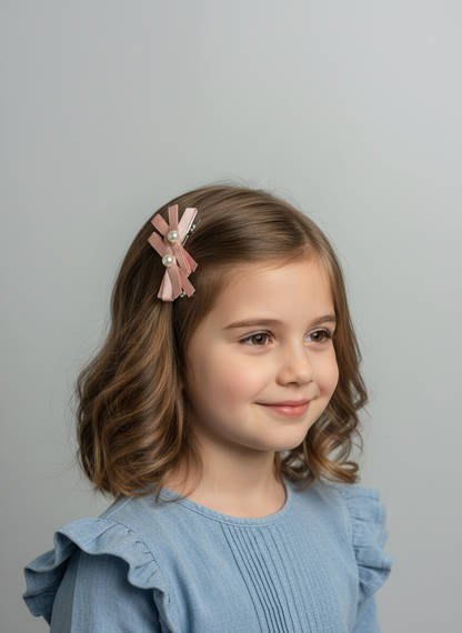 Young girl with a pink hair clip featuring a  layered bows and pearl centers against a gray background